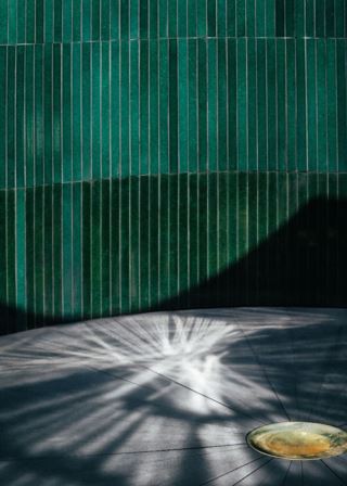 Area decorated with green lava stone tiles, with shadows on the floor and a golden feature in the foreground.