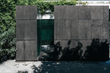 Exterior wall covered with dark lava stone tiles with an entrance leading to an interior space tiled in green.