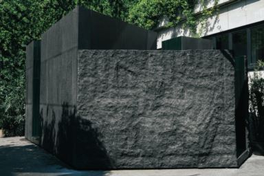 Exterior structure decorated with dark lava stone tiles and a rough stone wall, surrounded by greenery.