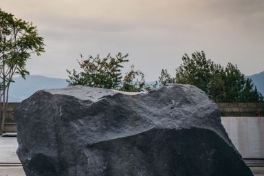 Large raw lava stone block outdoors, surrounded by trees and mountains in the background.